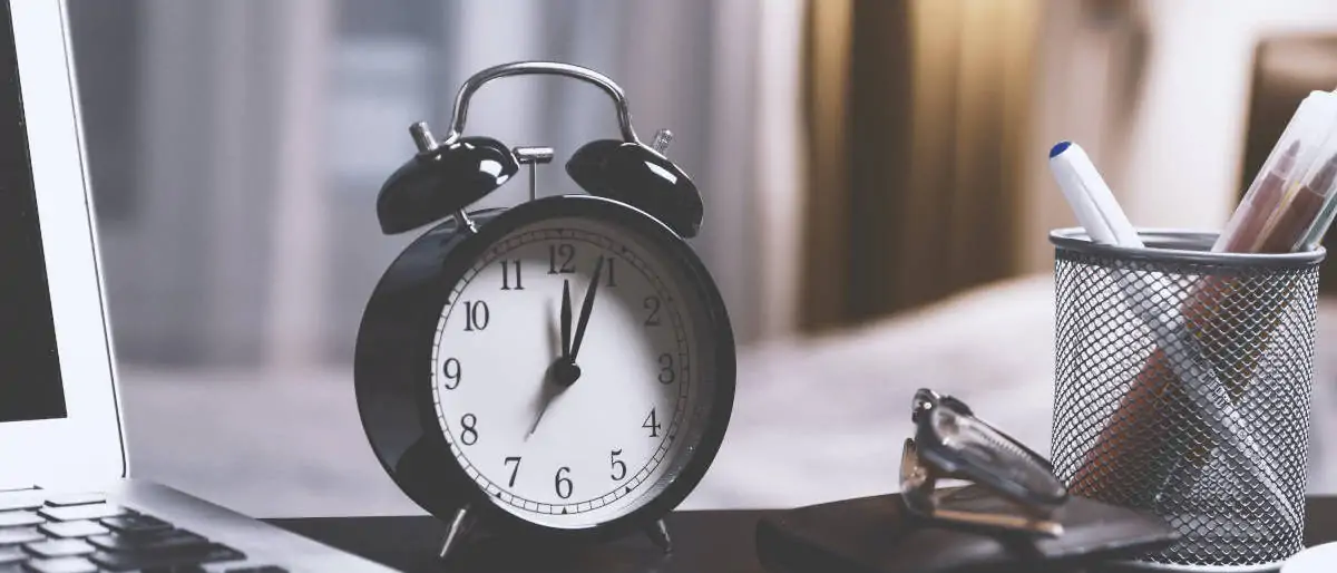 Twin bell alarm clock on a table with a laptop. Image by JESHOOTS.com.