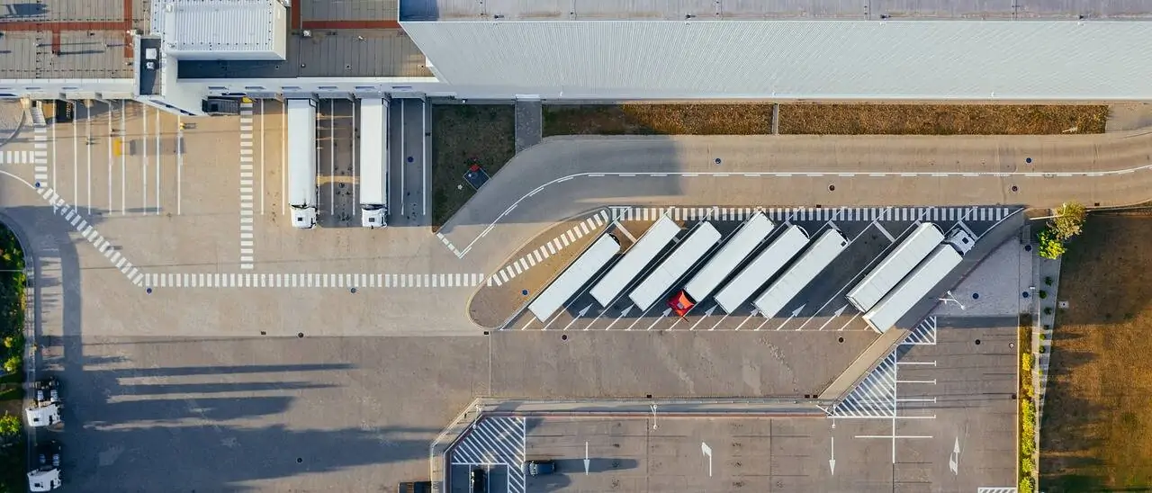 Logistikzentrum mit LKWs von oben - Titelbild Beitrag Avisieren, Avisierung, Avis – Definition und Überblick