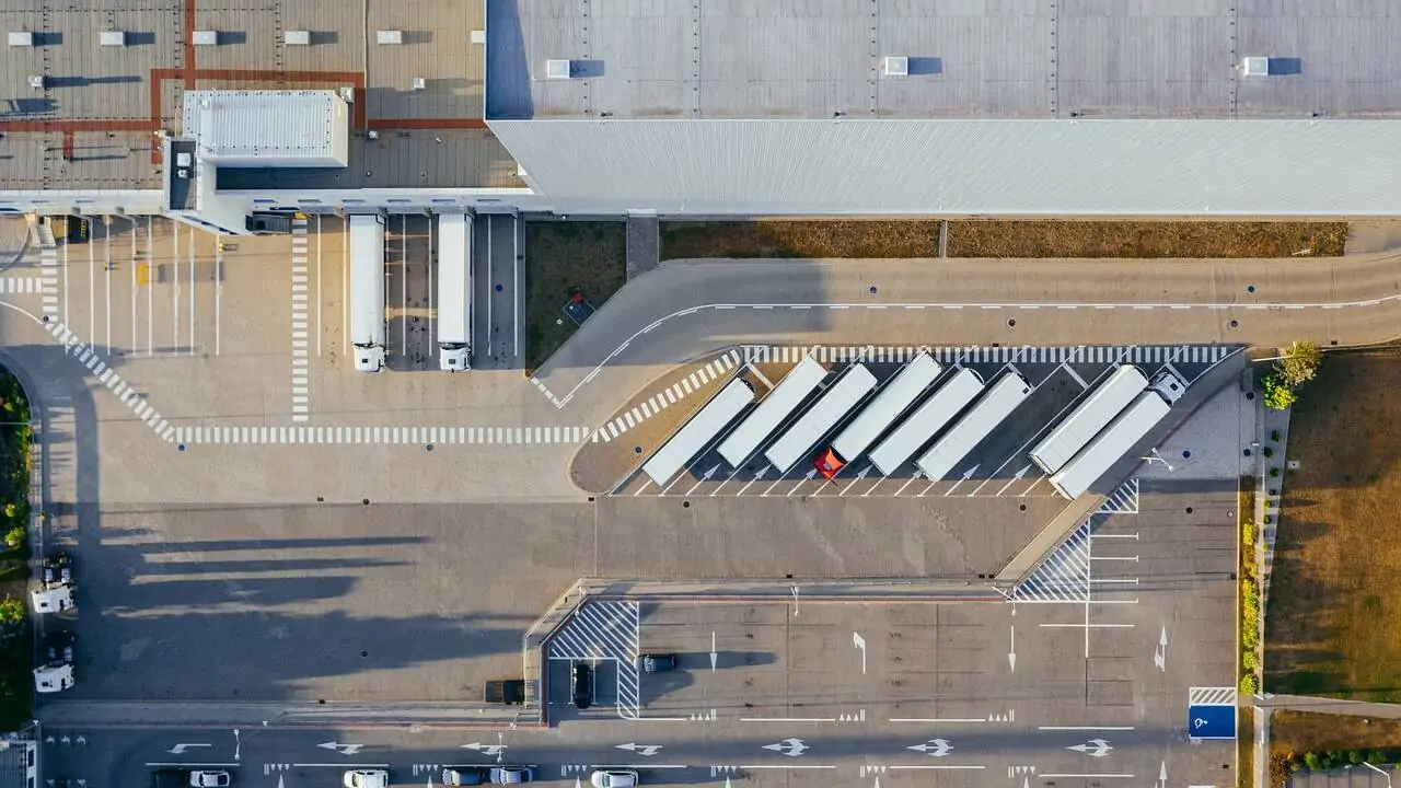 Logistikzentrum mit LKWs von oben - Titelbild Beitrag Avisieren, Avisierung, Avis – Definition und Überblick